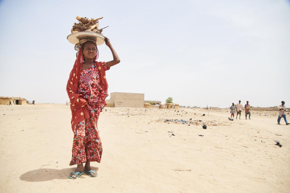 Nigerian woman stands in desert with basket of food balanced on her head