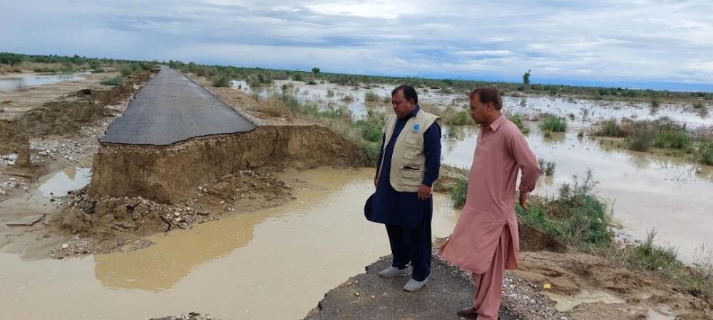 Two men survey a destroyed and flooded road