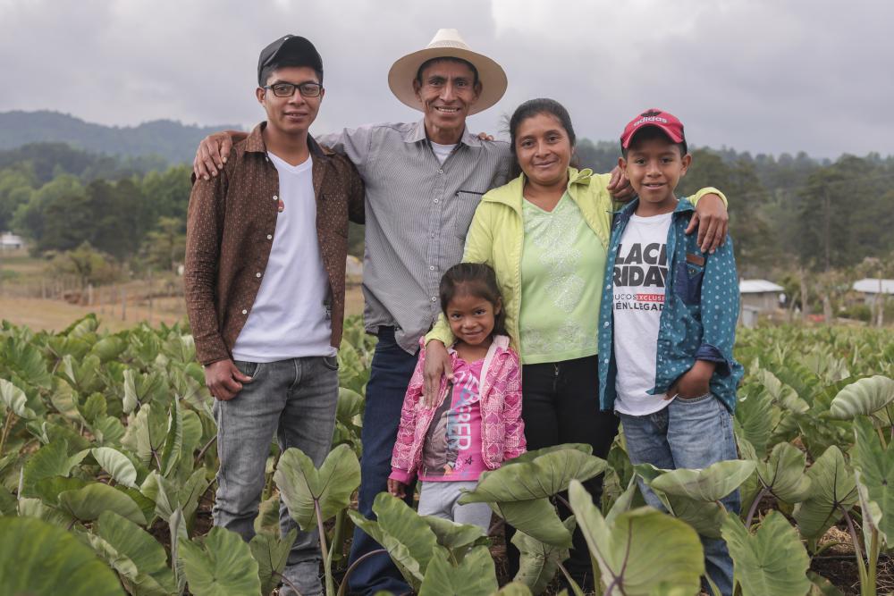 A family from Honduras stands among a field of crops