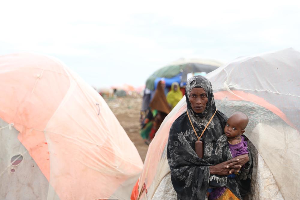 Woman standing in front of refugee tents holding baby