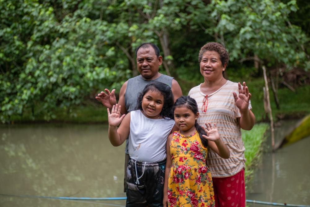 Family from Philippines stands in front of a river and waves