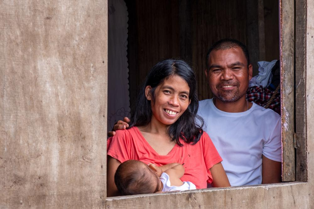 Woman and man from Philippines holding their baby smile out the window