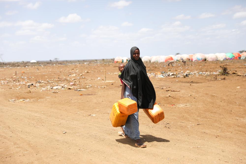 Woman from Somalia carries water buckets in the desert