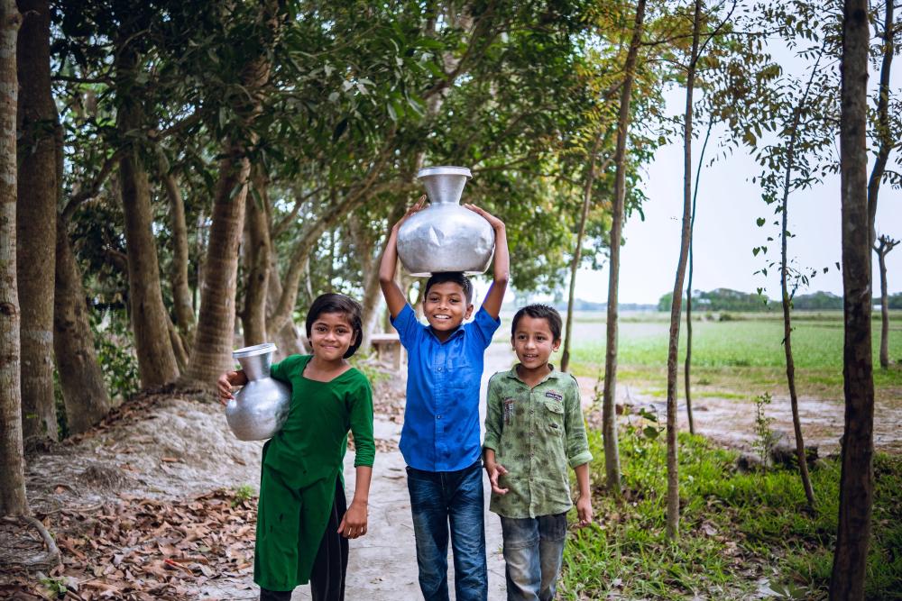 3 Bangladeshi children carry jugs of water