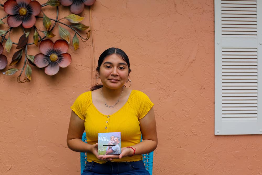 Woman from Honduras stands in front of house holding a CRS Rice Bowl
