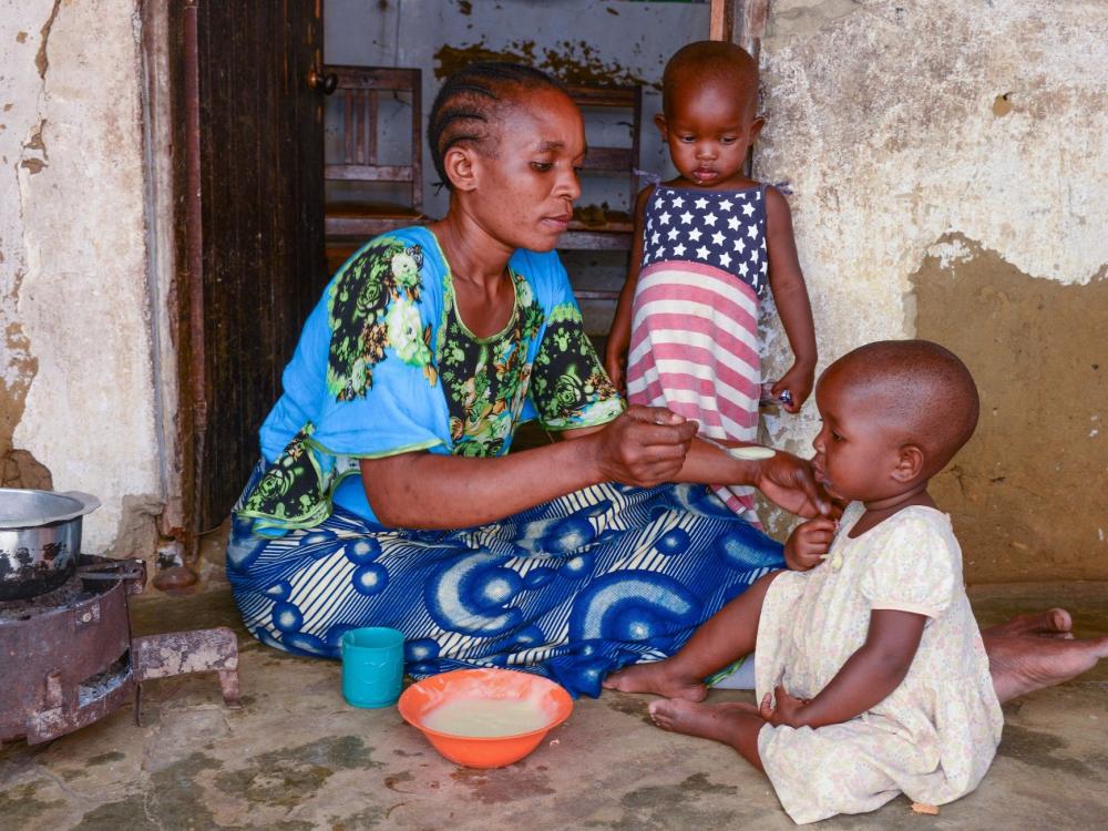 Woman sitting on the ground with her two daughters and feeding one of them