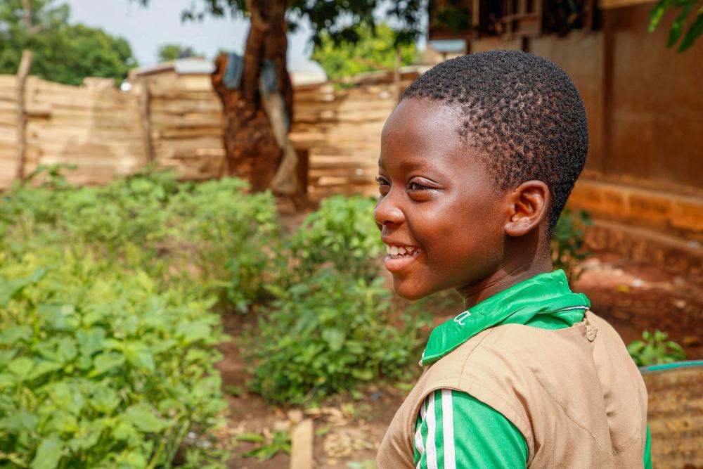 A young black girl in her school uniform looks back over her shoulder, smiling