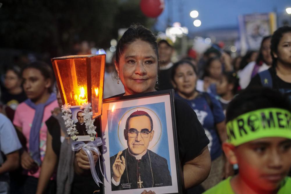 Woman holding a candle and a picture of Saint Óscar Romero.